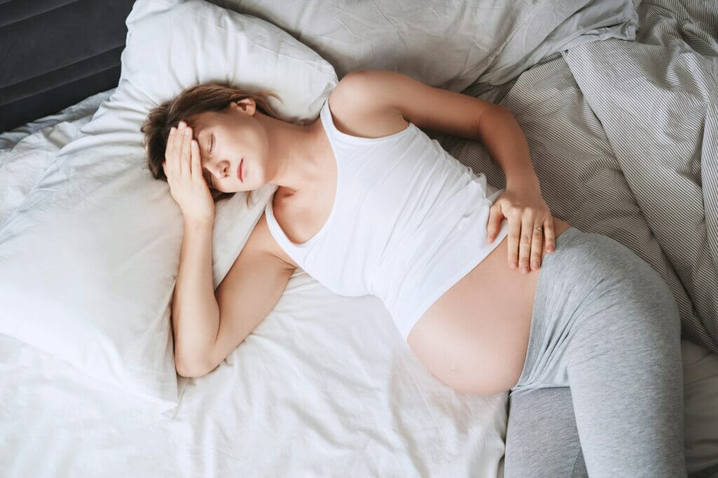 Exhausted pregnant woman suffering from insomnia or pain lying in bed.