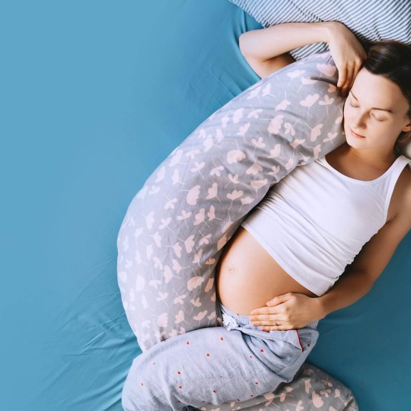 Pregnant woman relaxing or sleeping with belly support pillow in bed. Pregnancy concept.